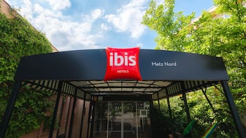 La entrada de un hotel con fachada de vidrio y un letrero rojo que indica que es un ibis hotel.
