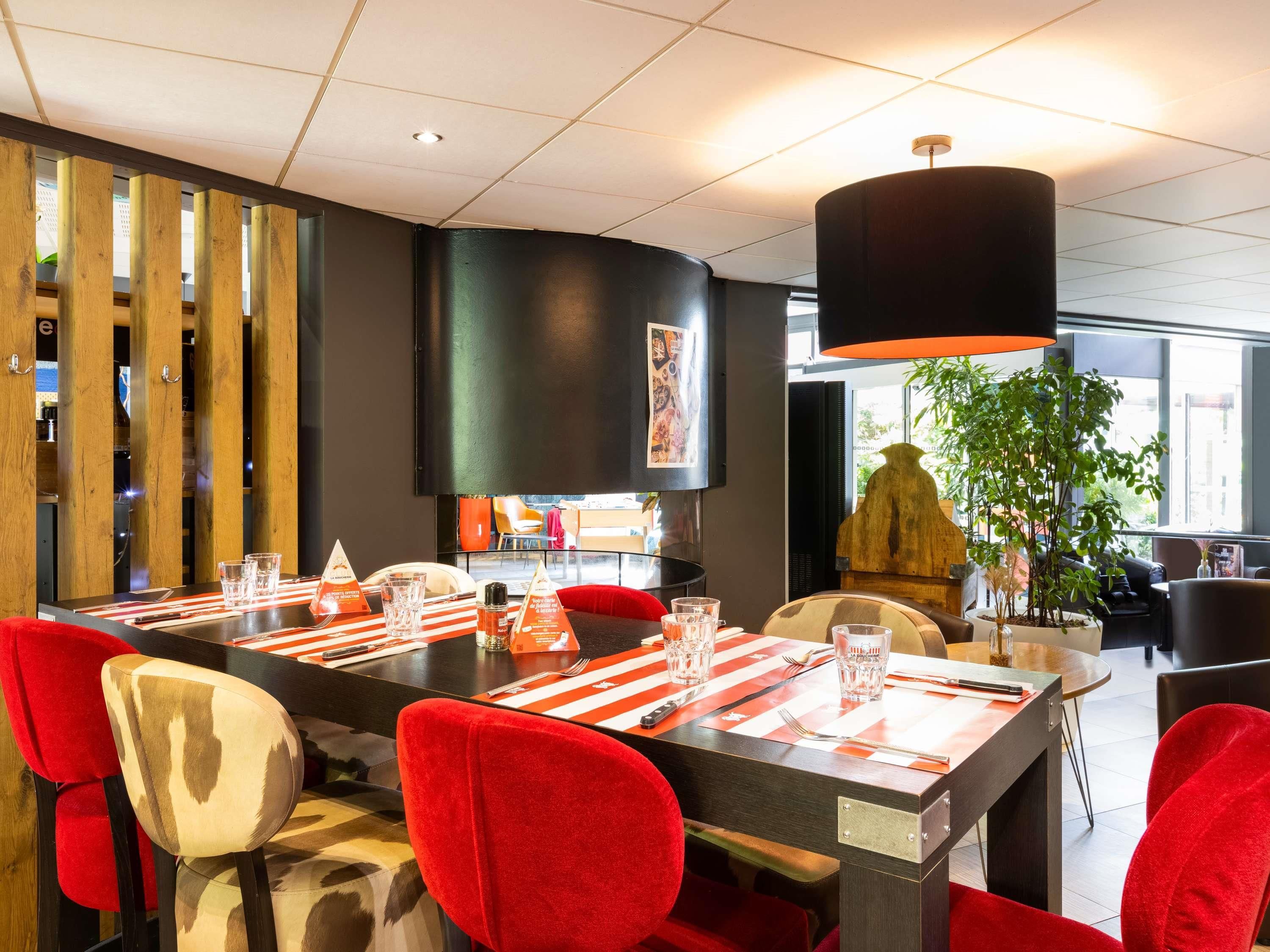Un espace de salle à manger moderne, avec une longue table, des chaises rouges et un grand luminaire suspendu noir.