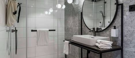 A modern bathroom with a glass-enclosed shower, a round mirror, a white sink, and a black vanity.