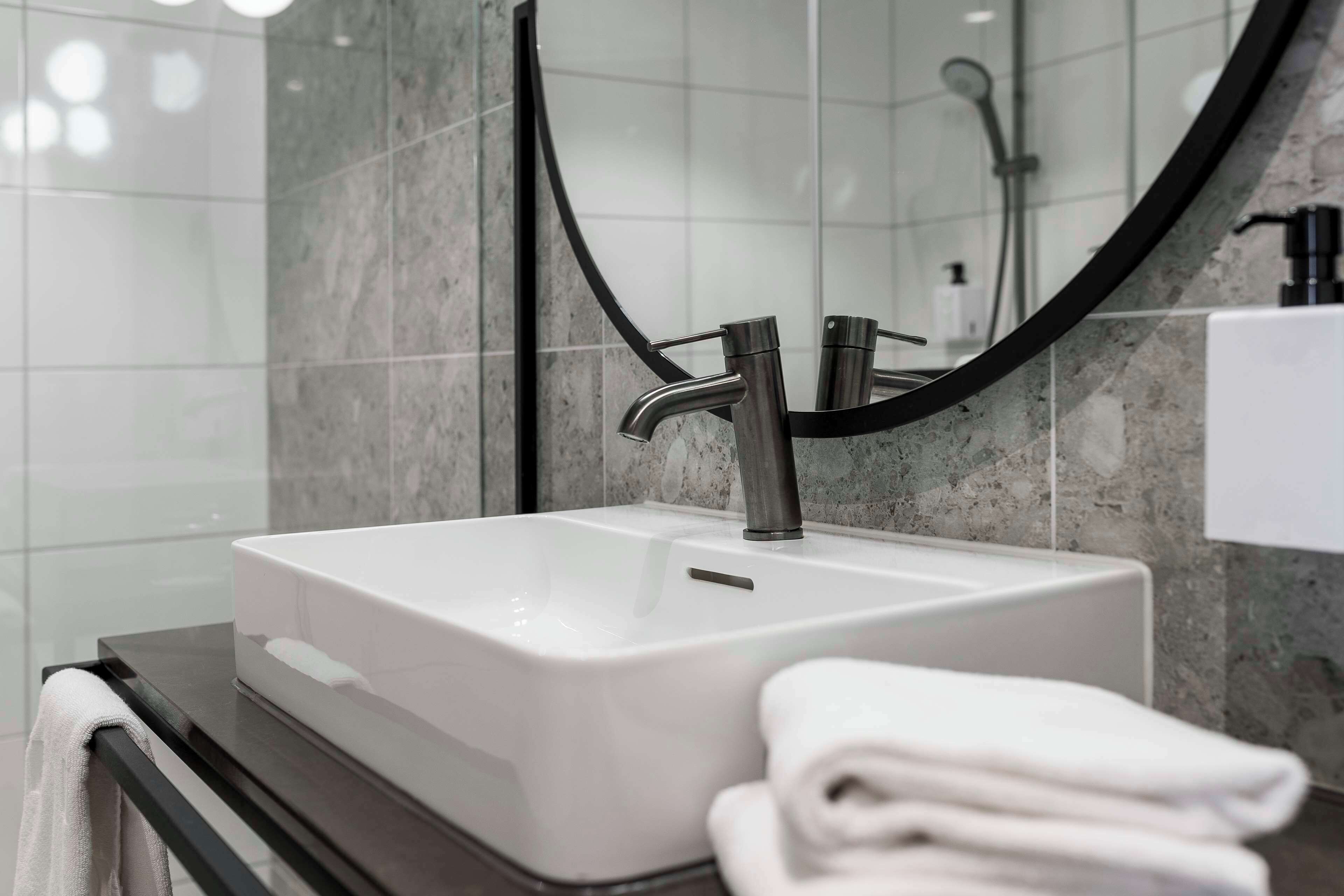 A modern bathroom with a white sink, a black faucet, and a towel on the counter.