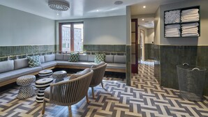 Un hall d’hôtel moderne avec un canapé d’angle, des poufs à motifs, un sol à chevrons et un porte-serviettes fixé au mur.
