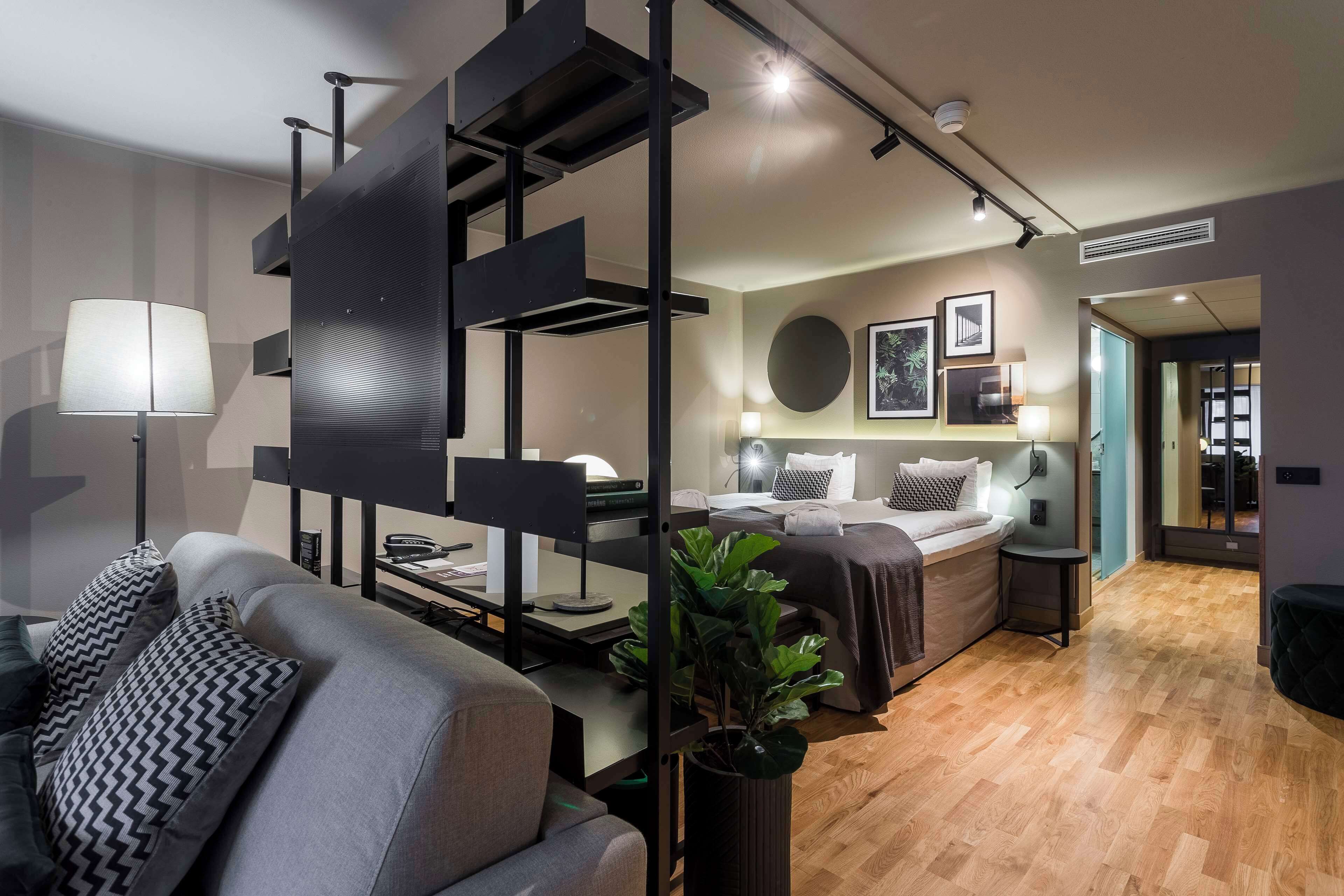 Habitació d'hotel moderna amb un sofà, escriptori, llit i una planta gran.