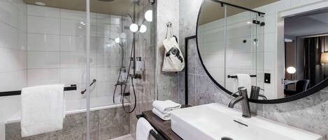 Un baño moderno con ducha de vidrio, un espejo grande y un lavamanos blanco.