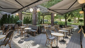 Un café en plein air avec des meubles en osier, des tables rondes et un espace salon abrité.