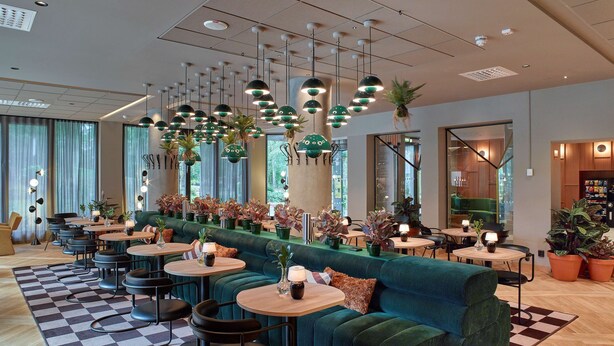 Un intérieur moderne avec un canapé vert, des tables rondes et des lampes vertes suspendues.
