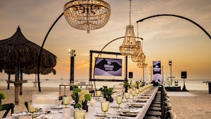 A beachside dining setup with a long table, elegant chandeliers, and a Hilton sign in the background. - Hilton Aruba Caribbean Resort and Casino (Noord)