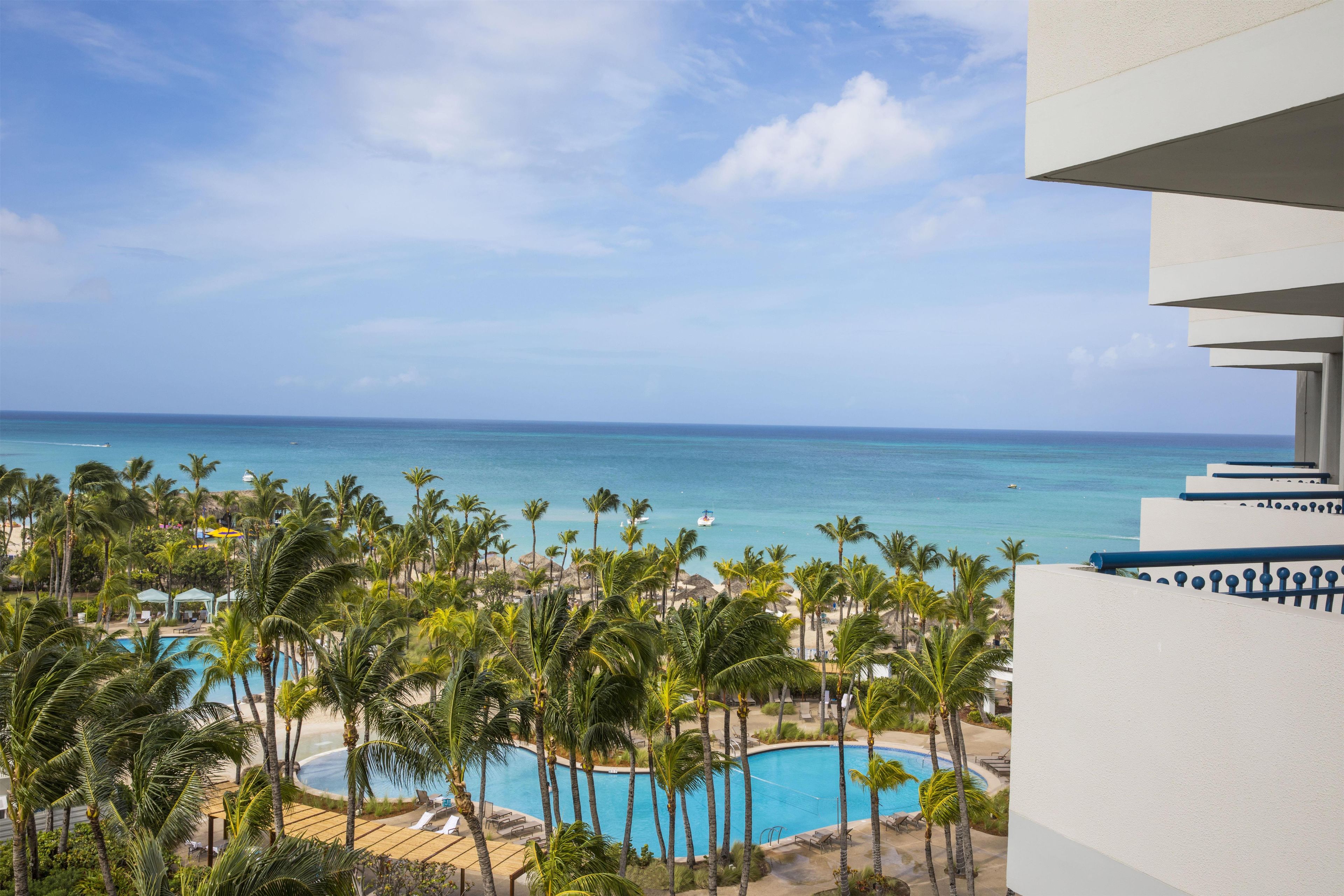 Un resort con piscina rodeada de palmeras y vista al océano.