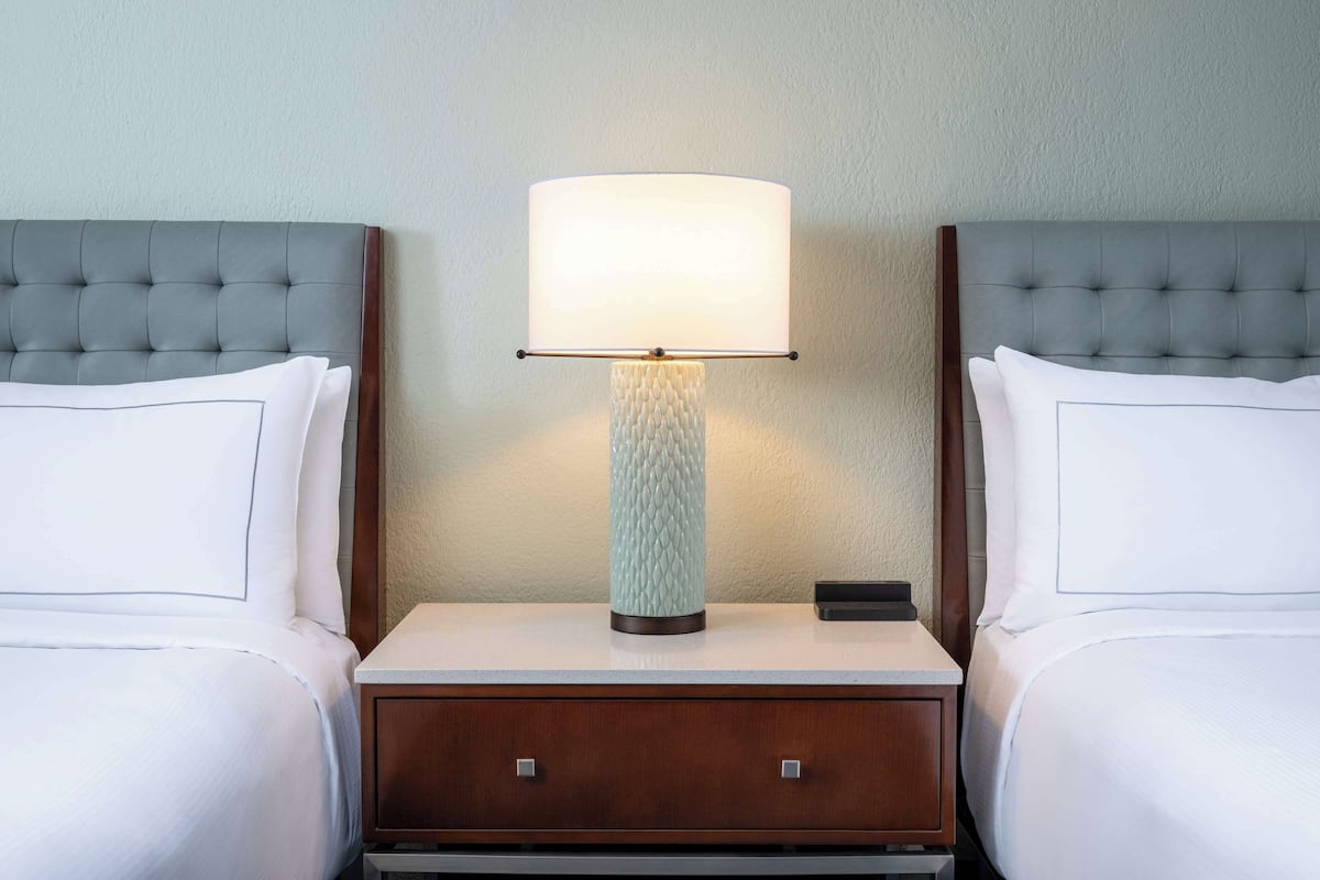 A hotel room with two beds, a nightstand with a lamp, and a wooden drawer unit.