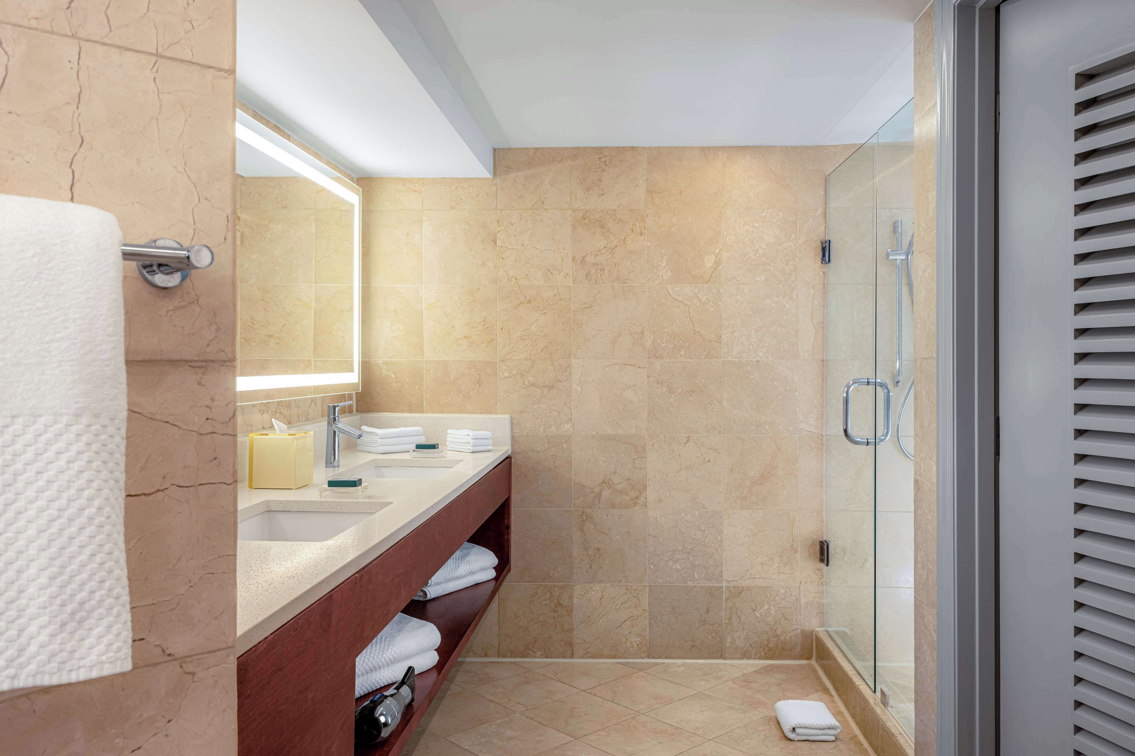 Un baño moderno con piso de mármol, cabina de ducha de vidrio y tocador con espejo y perchero.