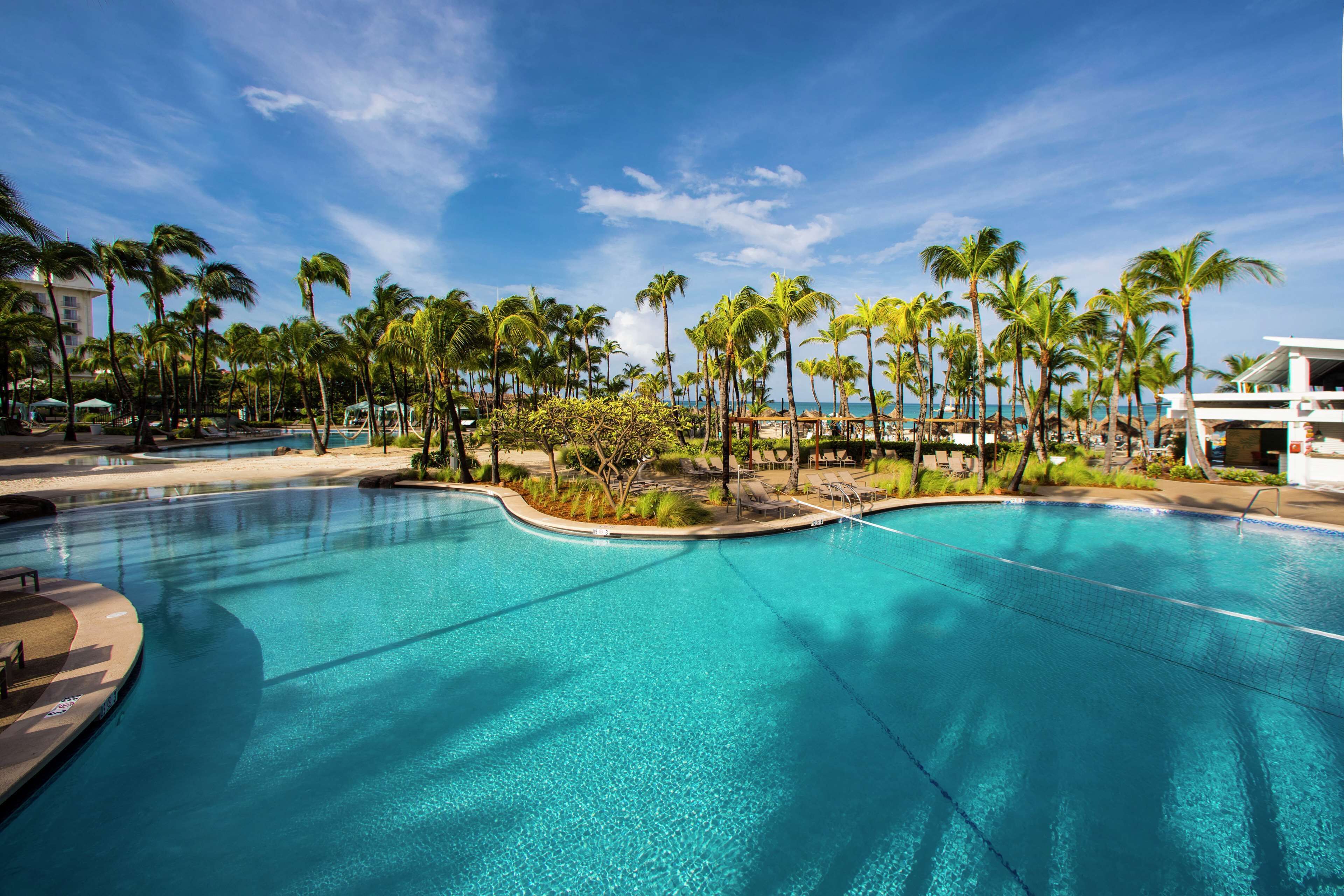 Una piscina grande y cristalina rodeada de palmeras y un edificio de resort.