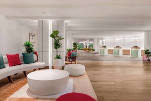 A spacious lobby with a modern design, featuring a seating area with sofas and ottomans, a reception desk, and potted plants.