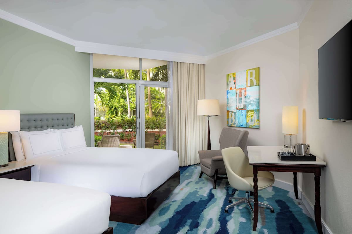A hotel room with a large bed, a desk with a chair, a TV, and a window with curtains.