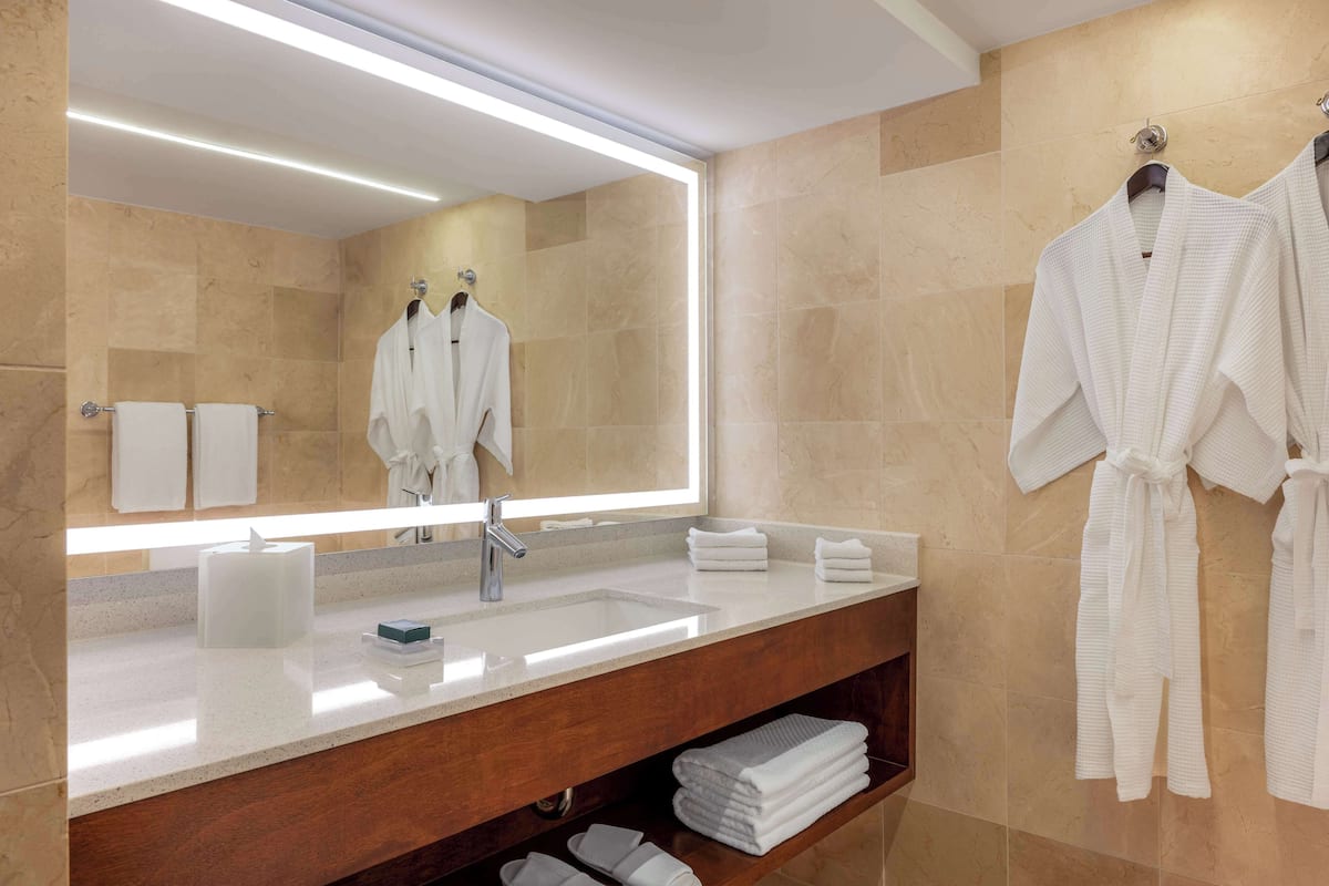 A modern bathroom with a large mirror, a sink, and a vanity. There are towels and robes hanging on the wall.