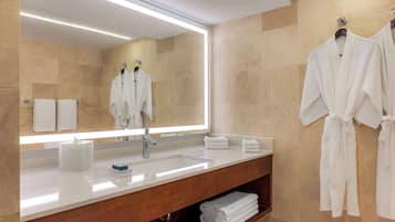 Une salle de bain moderne avec un grand miroir, un lavabo et un meuble-lavabo. Des serviettes et des peignoirs sont accrochés au mur.