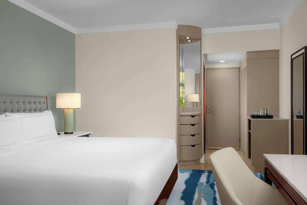 A hotel room with a large bed, a desk, a chair, a dresser, and a mirror.