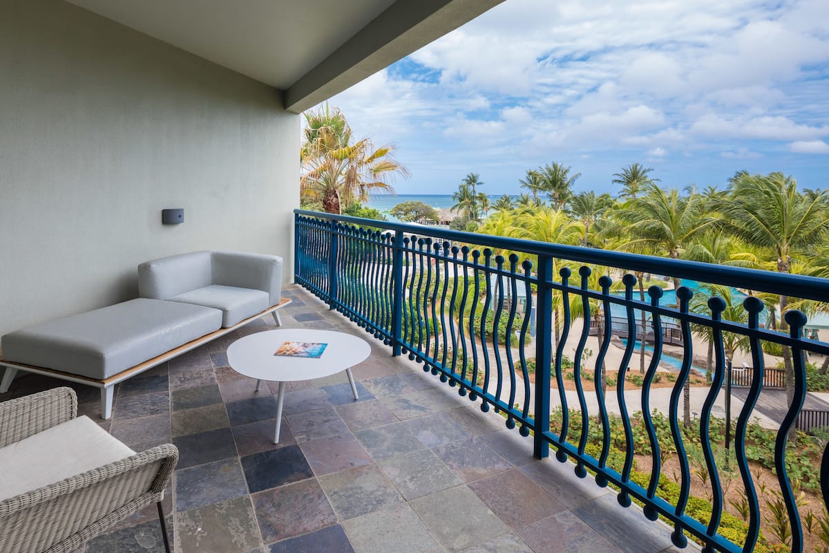 A balcony with a blue railing, a grey sofa, a small round table, and a wicker chair.