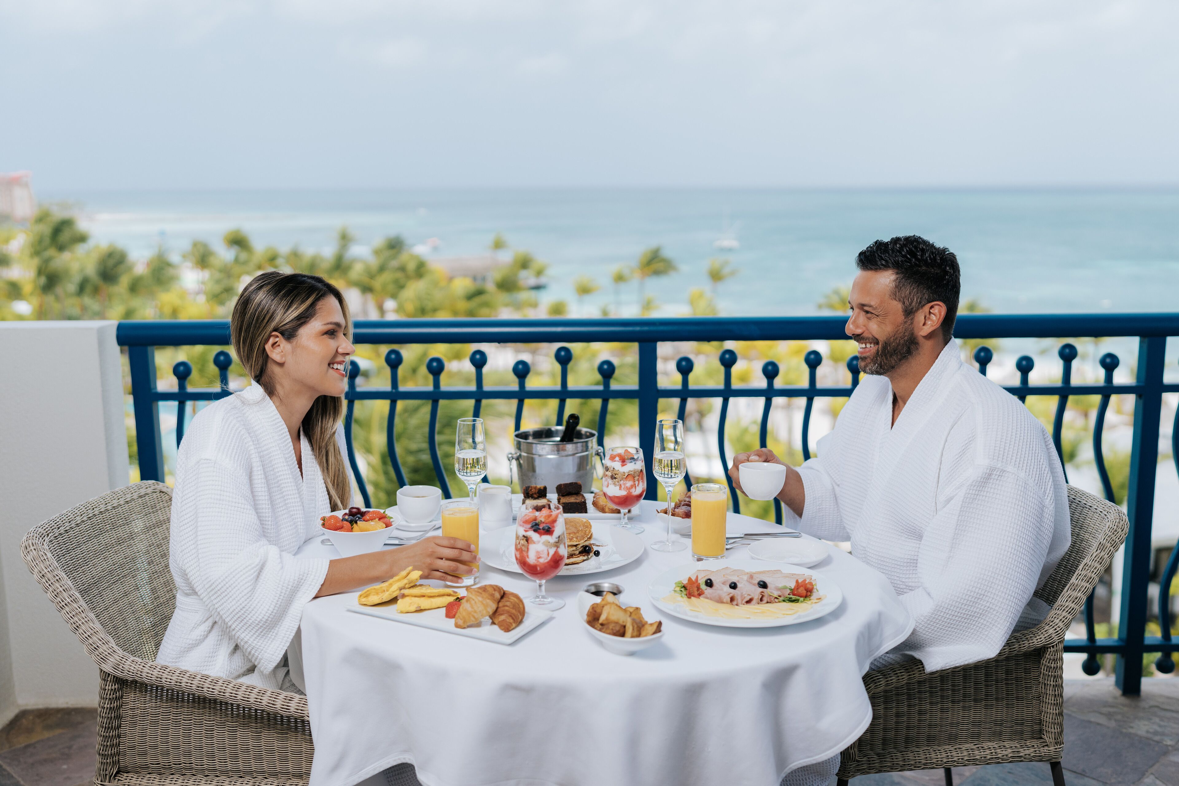 A couple dining at a table with a view of the ocean, featuring breakfast items and drinks.