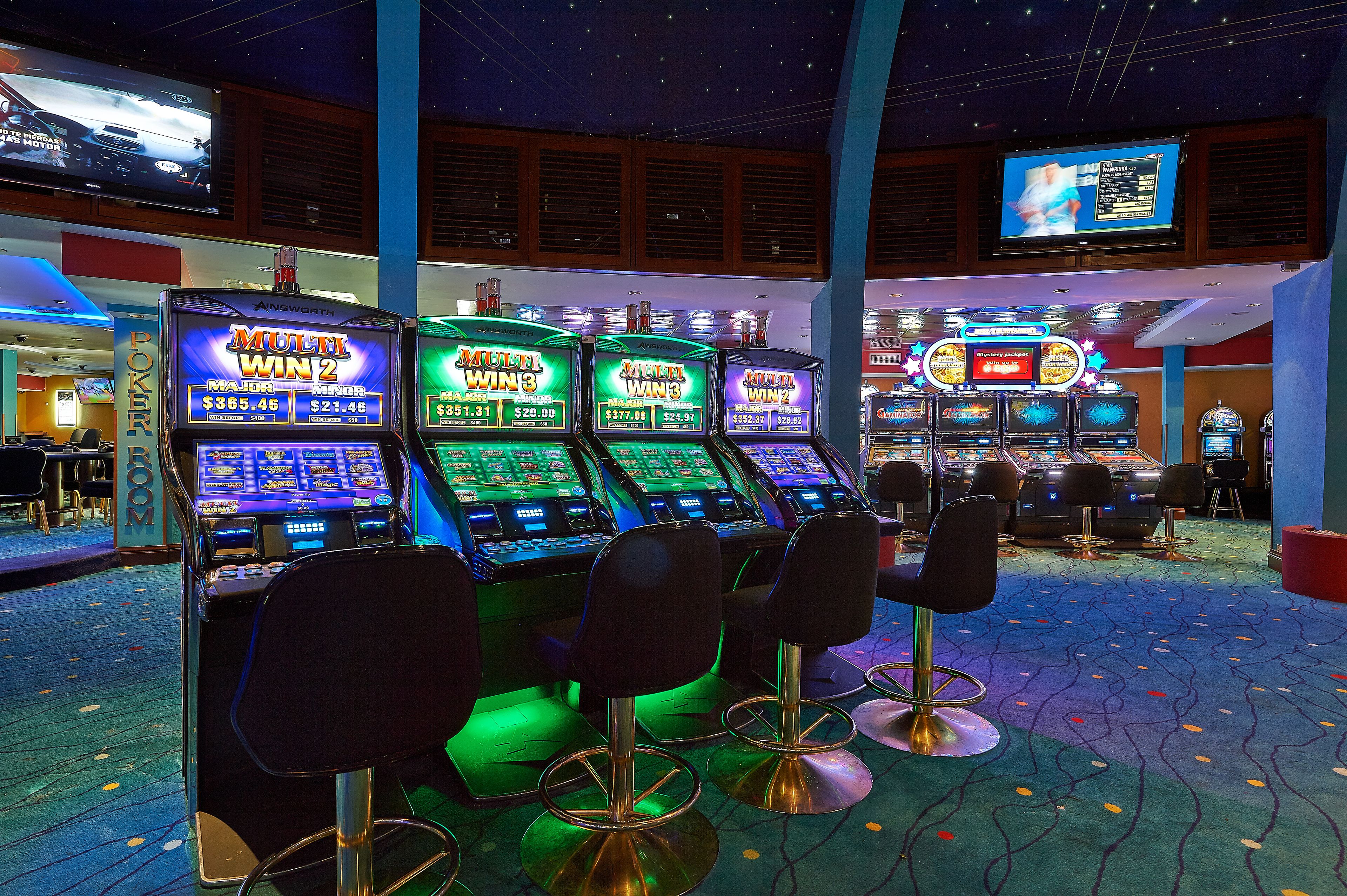 Ein Casino-Bereich mit Spielautomaten, Barhocker und einem Fernseher, der Spielinformationen anzeigt.
