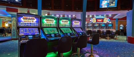 Ein Casino-Bereich mit Spielautomaten, Barhocker und einem Fernseher, der Spielinformationen anzeigt.