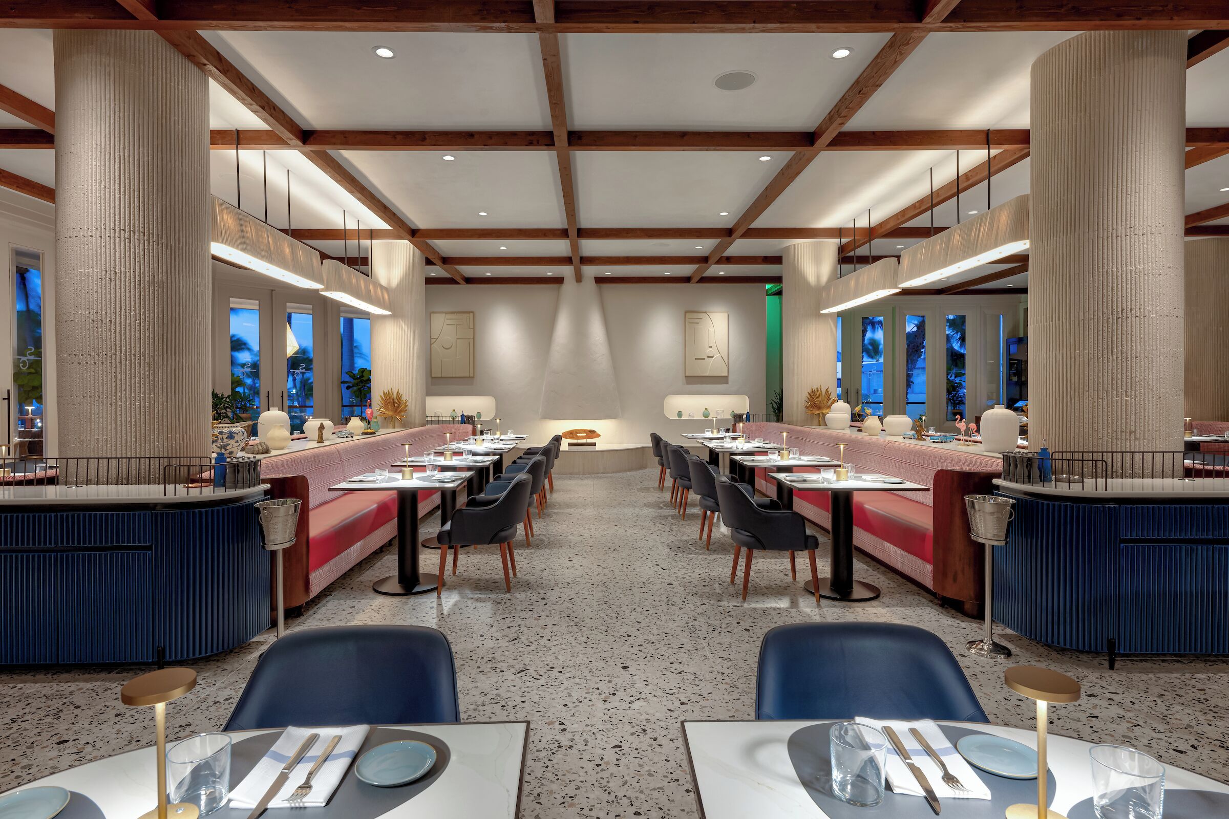 A spacious restaurant with high ceilings, exposed beams, and a central seating area with tables and chairs.
