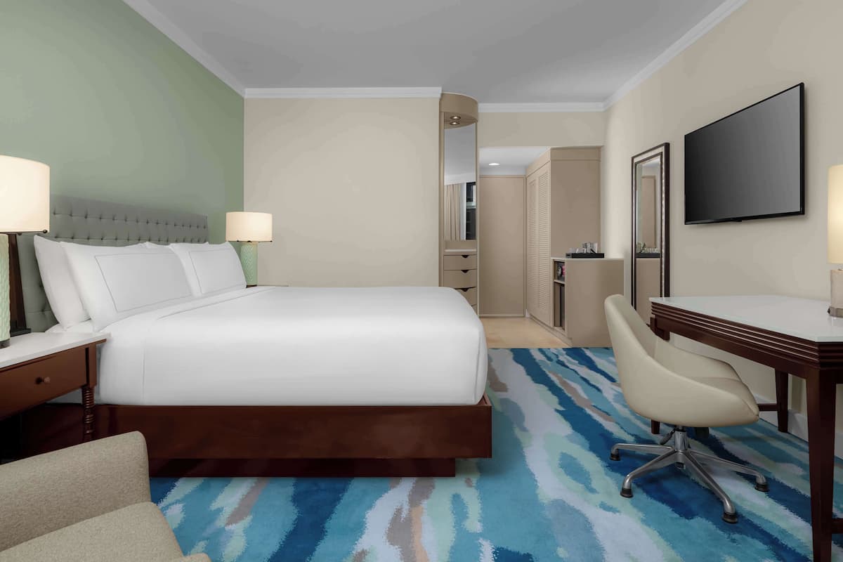 A hotel room with a large bed, a desk, a chair, a TV, and a mirror.