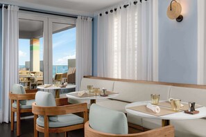 A modern dining area with round tables, cushioned chairs, and a view of the sea.