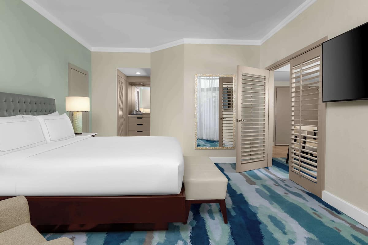 A hotel room with a large bed, a bedside table, a lamp, a bench, a TV, and a wardrobe.