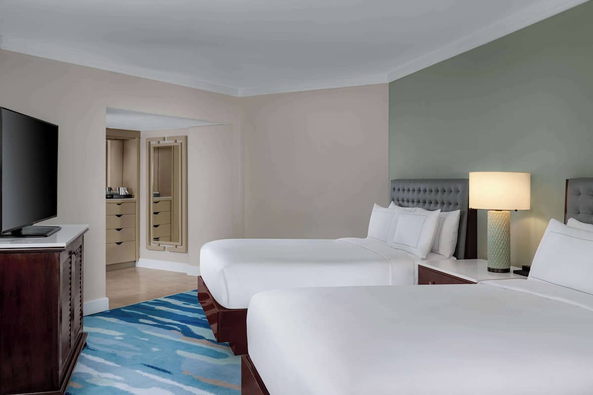 A hotel room with two beds, a TV, a lamp, and a wardrobe.
