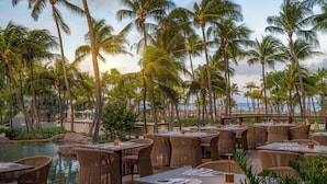 An outdoor dining area with wicker furniture, a pool, and palm trees. - Hilton Aruba Caribbean Resort and Casino (Noord)