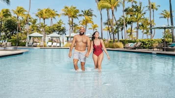 A couple walking in a pool surrounded by palm trees.