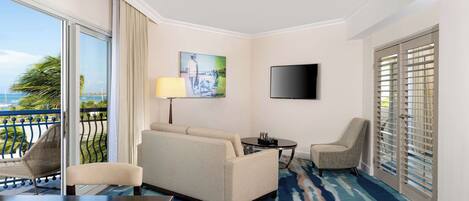 A hotel room with a balcony, a sofa, a chair, a TV, and a painting.