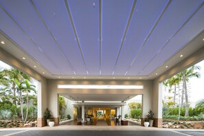 A modern hotel entrance with a covered walkway, palm trees, and a central seating area. - Hilton Aruba Caribbean Resort and Casino (Noord)