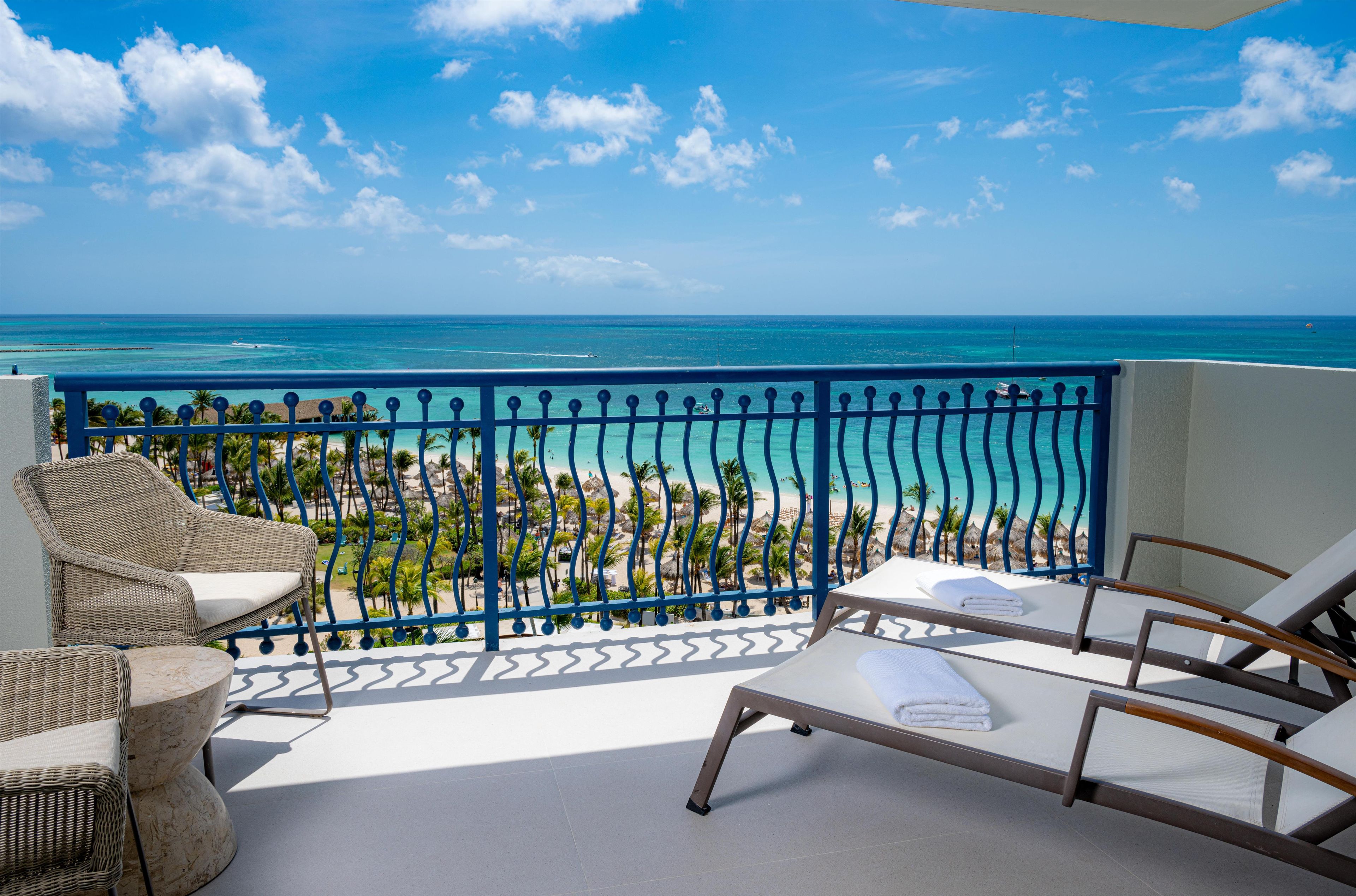 A balcony with wicker furniture, a view of the beach, and the ocean.