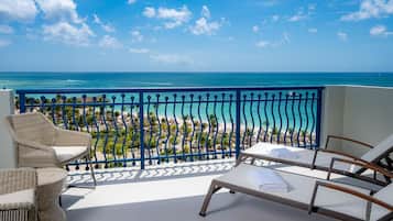 A balcony with wicker furniture, a view of the beach, and the ocean.