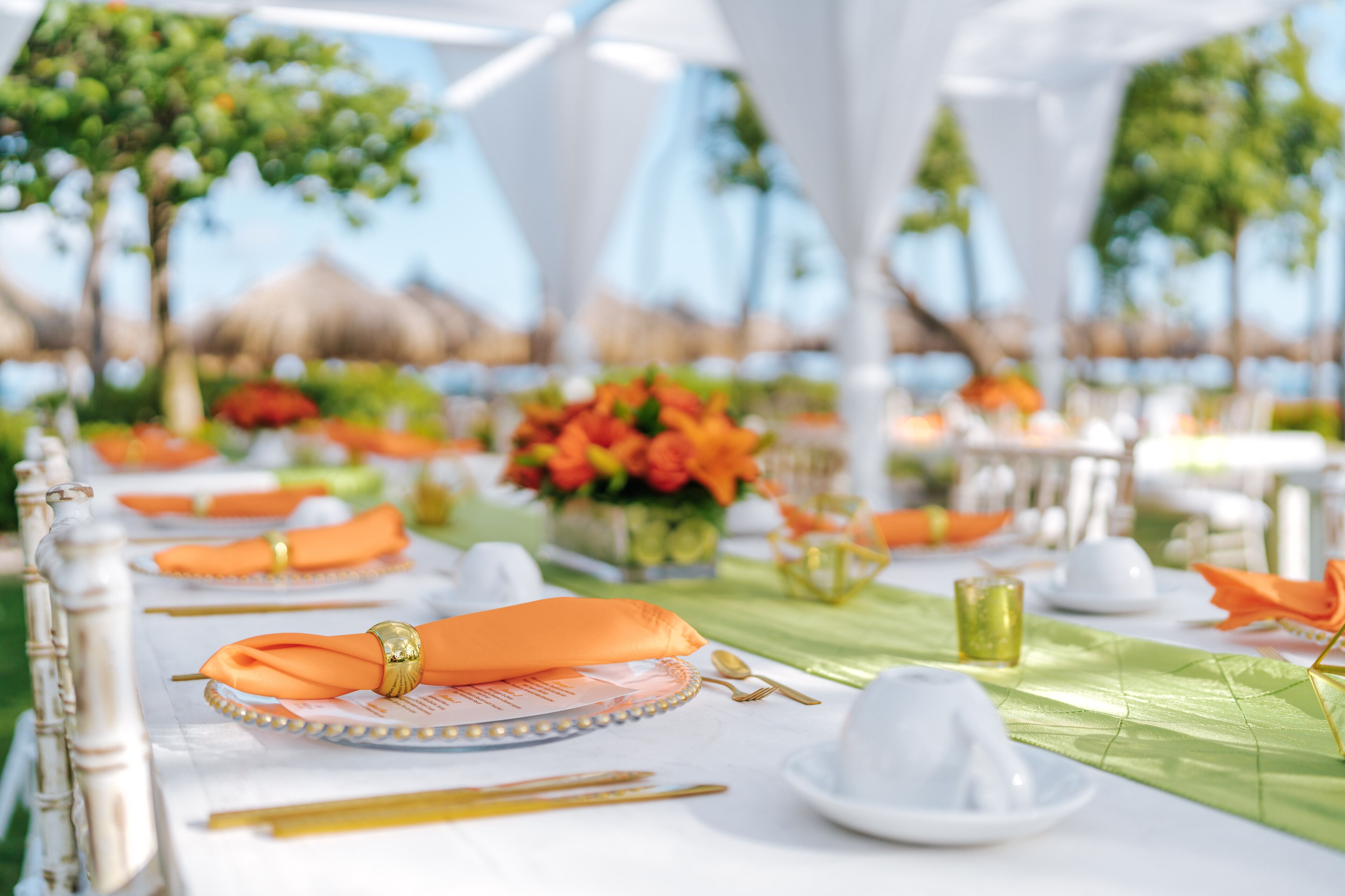 A table set for a meal with white tablecloths, orange napkins, and gold cutlery.