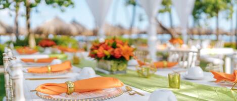 A table set for a meal with white tablecloths, orange napkins, and gold cutlery.