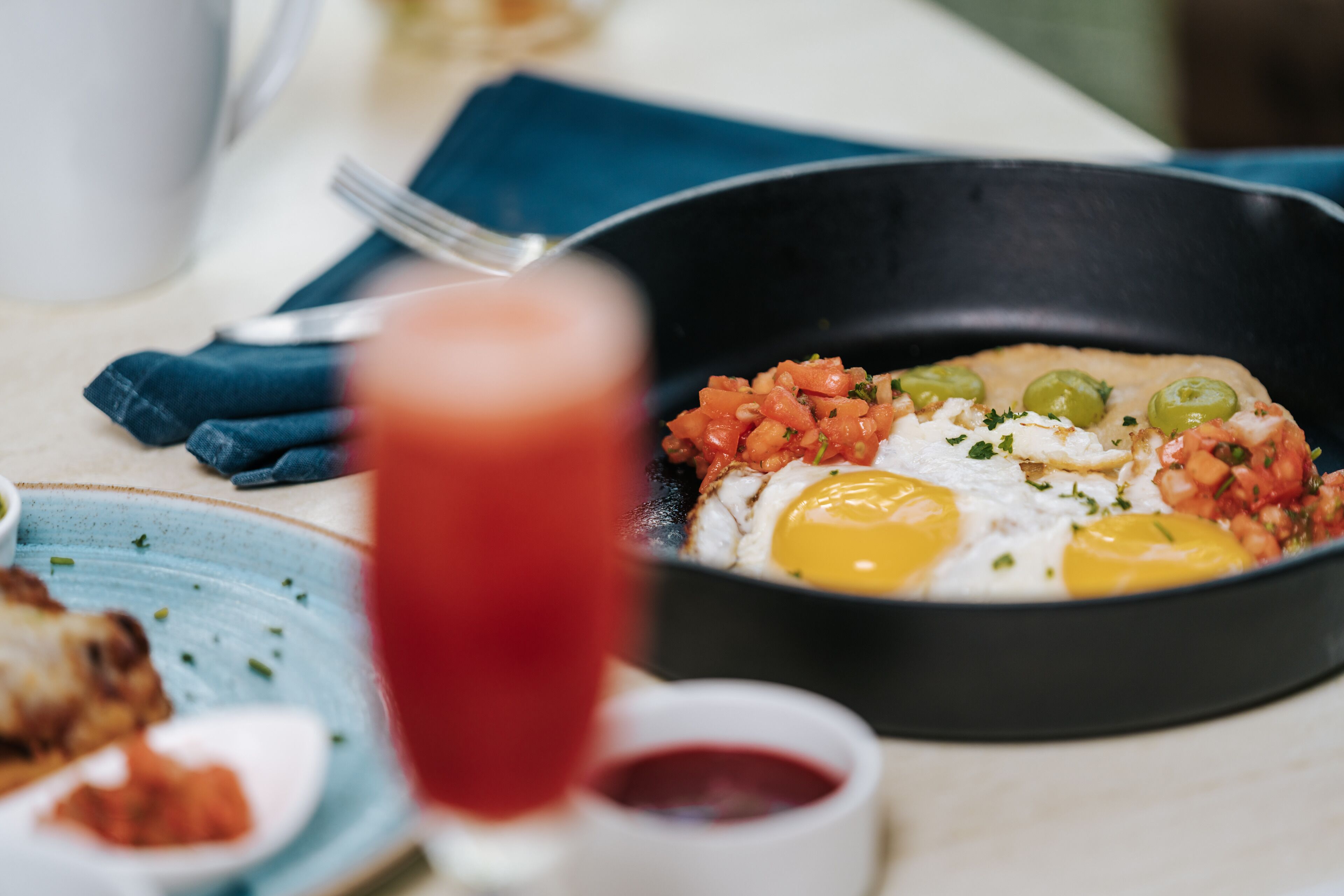 A breakfast plate with eggs, tomatoes, and green olives.