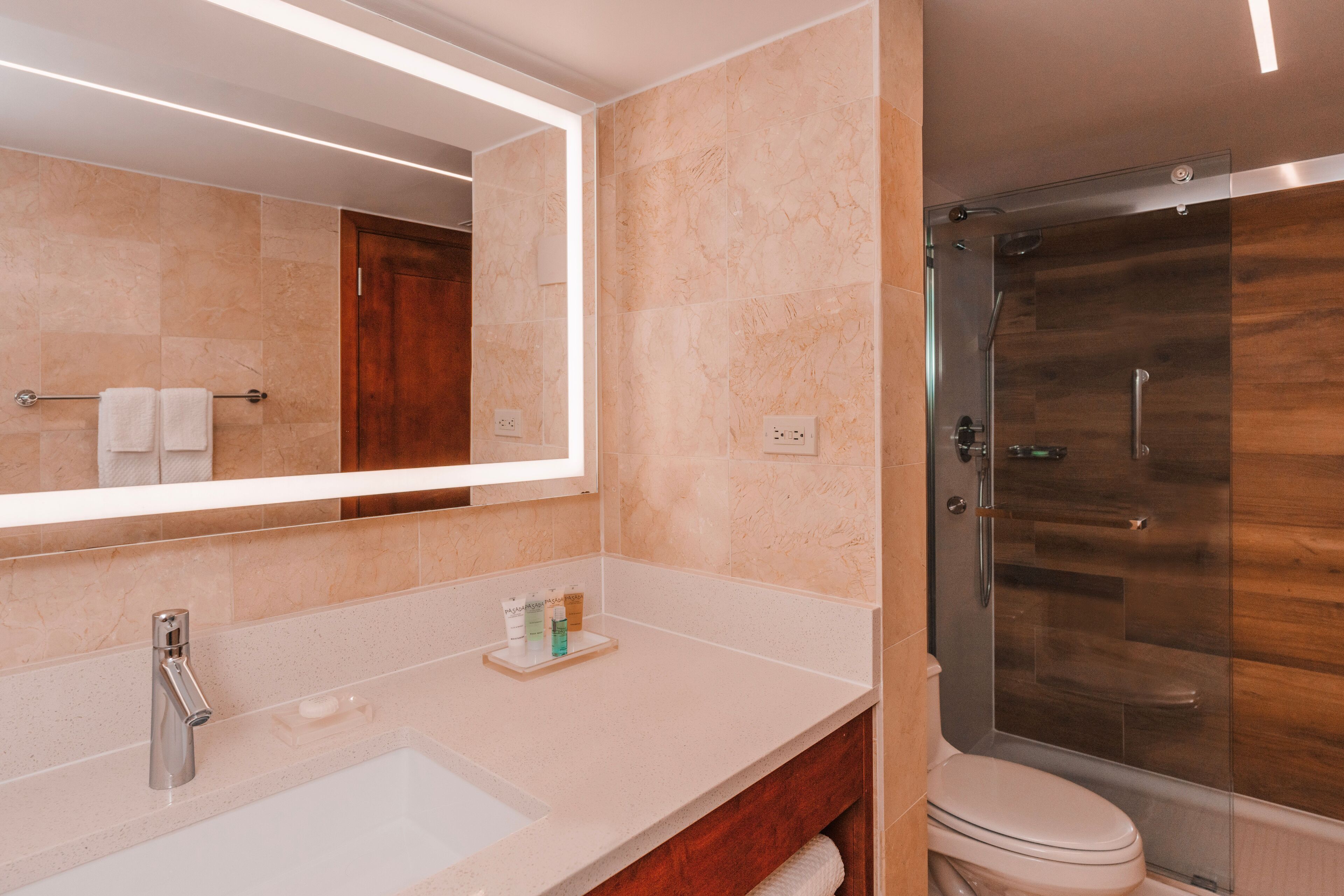 A modern bathroom with a large mirror, a sink, a toilet, and a glass-enclosed shower.