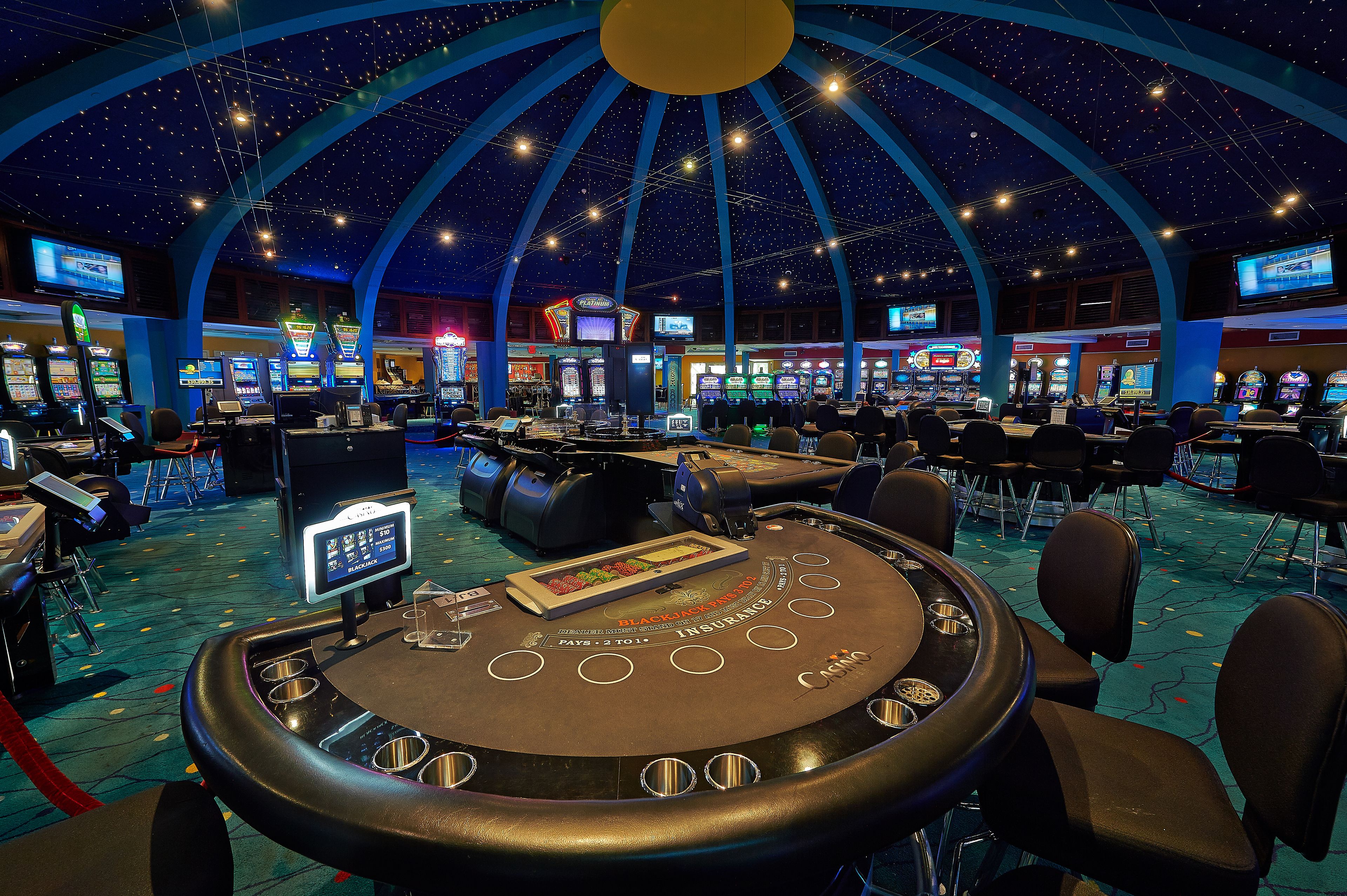 Ein Casino mit mehreren Spieltischen und Spielautomaten unter einer sternenübersäten Kuppel.