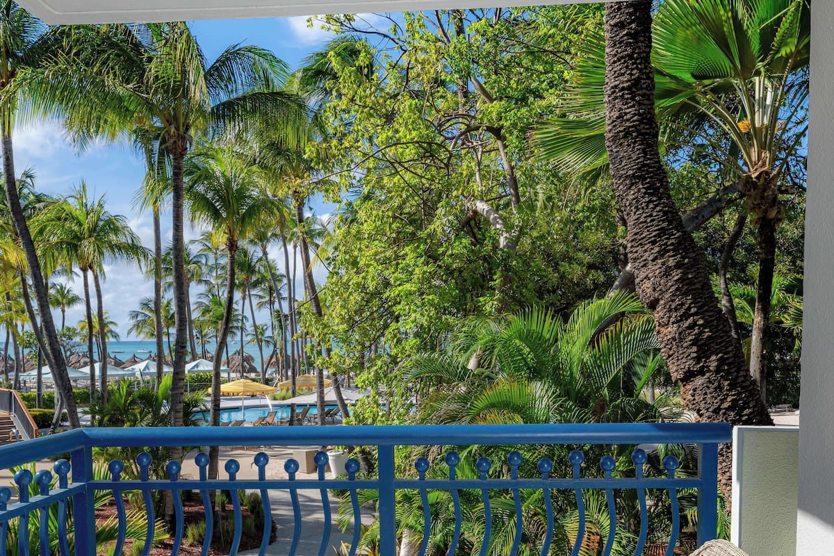 A balcony with wicker furniture and a view of palm trees and the ocean.