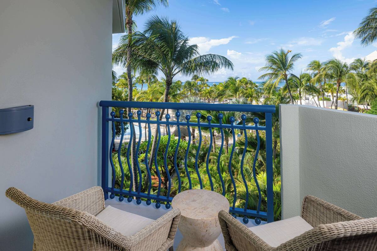 A balcony with wicker furniture and a view of palm trees and a beach.