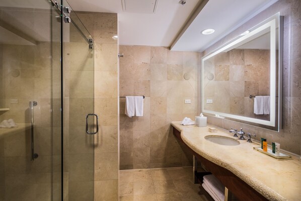 Un baño moderno con ducha de vidrio, lavamanos con encimera de mármol y un espejo grande.