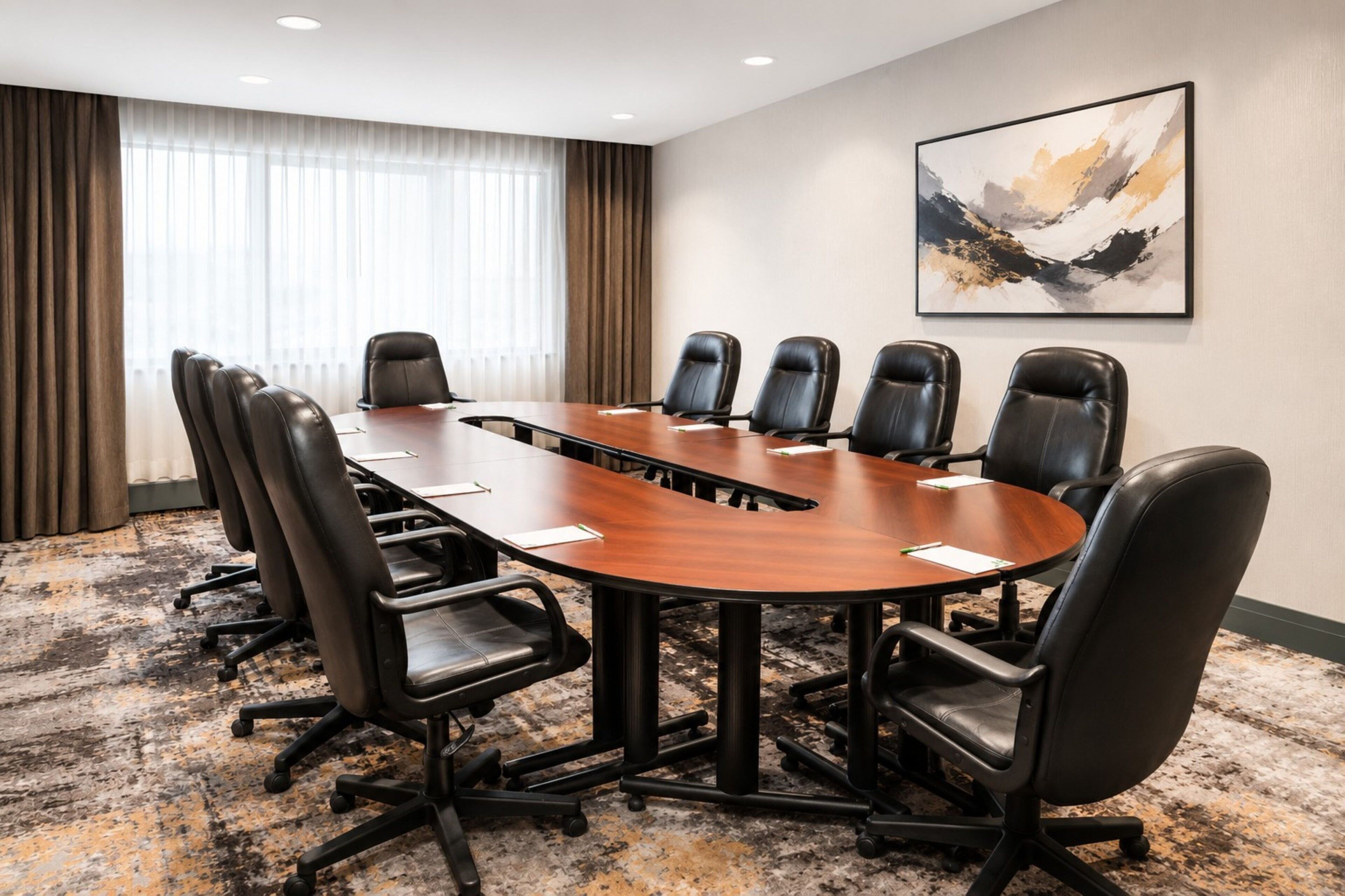 A conference room with a large oval table, black leather chairs, a carpeted floor, and a painting on the wall.
