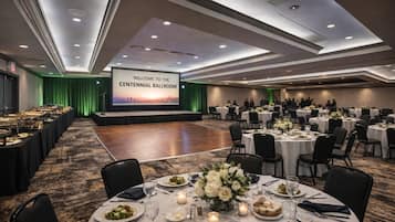 A spacious ballroom with a stage, multiple round tables set for dining, and a large screen displaying a welcome message.