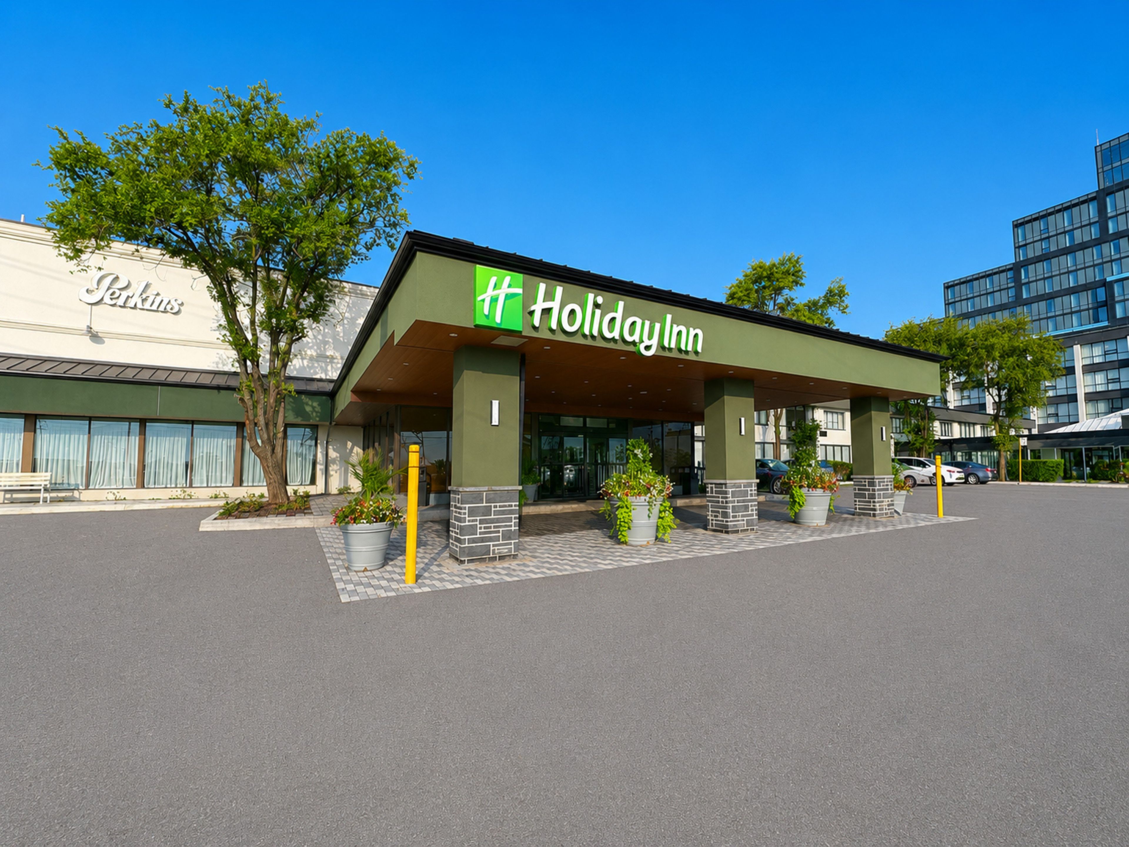 A Holiday Inn hotel with a green facade, large windows, and potted plants in front.