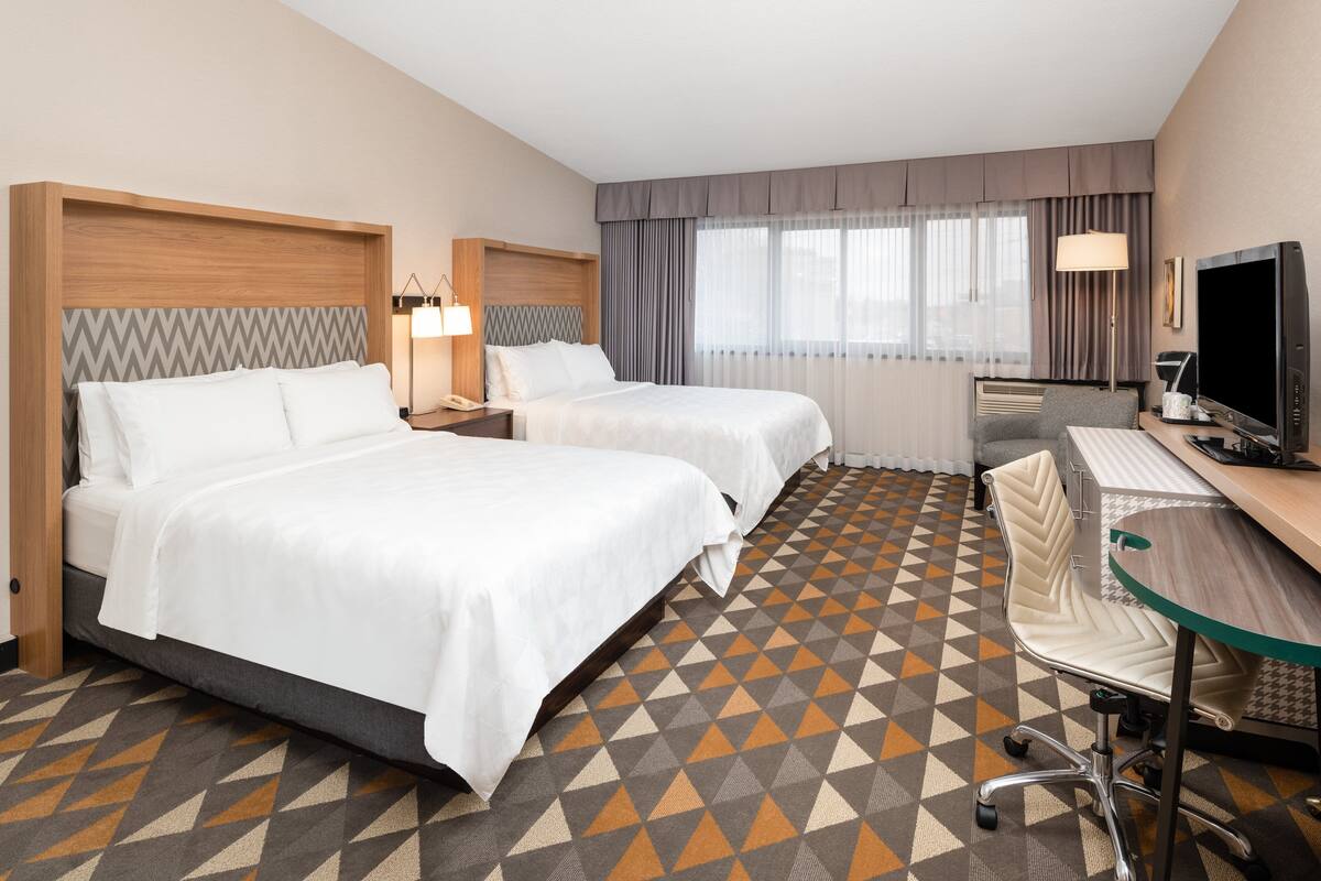 A hotel room with two beds, a desk, a chair, and a TV.