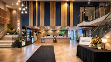 A modern hotel lobby with a reception desk, a staircase, and a view of the upper floor.
