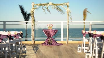 Montagem de cerimônia de casamento com um arco decorado e mesas, com vista para o oceano.