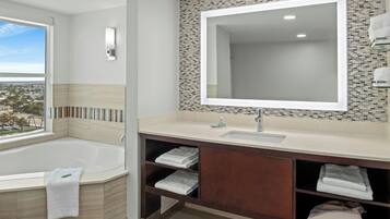 A modern bathroom with a large bathtub, a vanity with a mirror, and a view of the city.