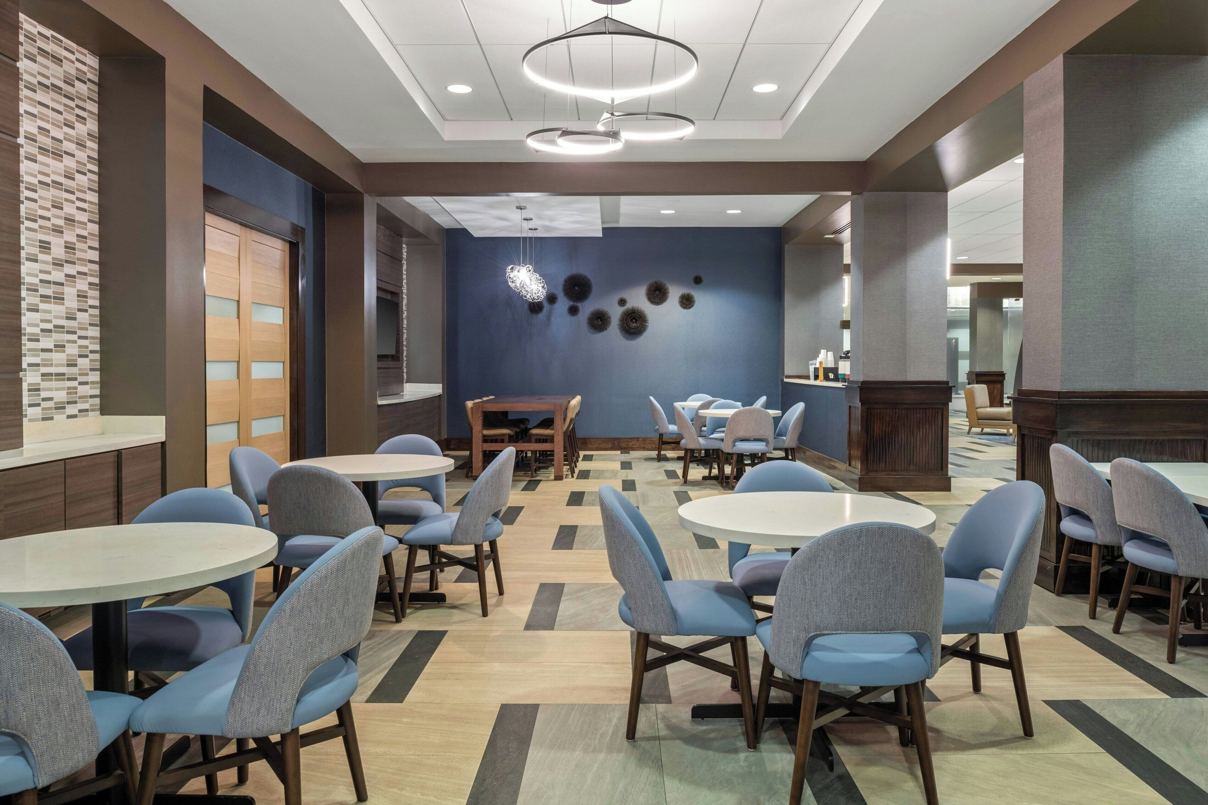 A modern dining area with round tables and blue chairs, a wooden cabinet, and a blue wall with decorative elements.